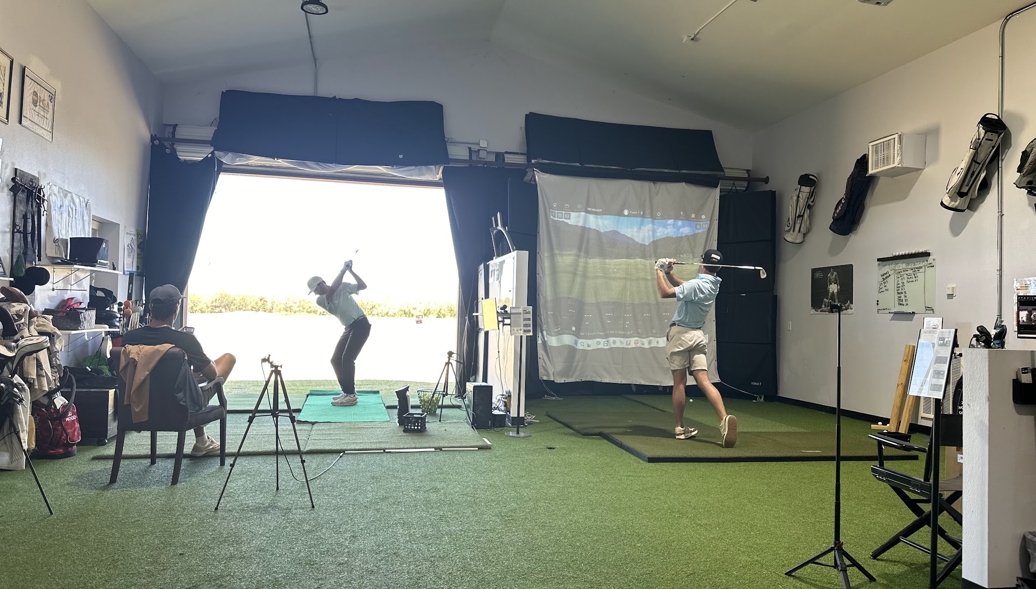 Two golfers practicing in adjacent indoor hitting bays at Golf Performance Group