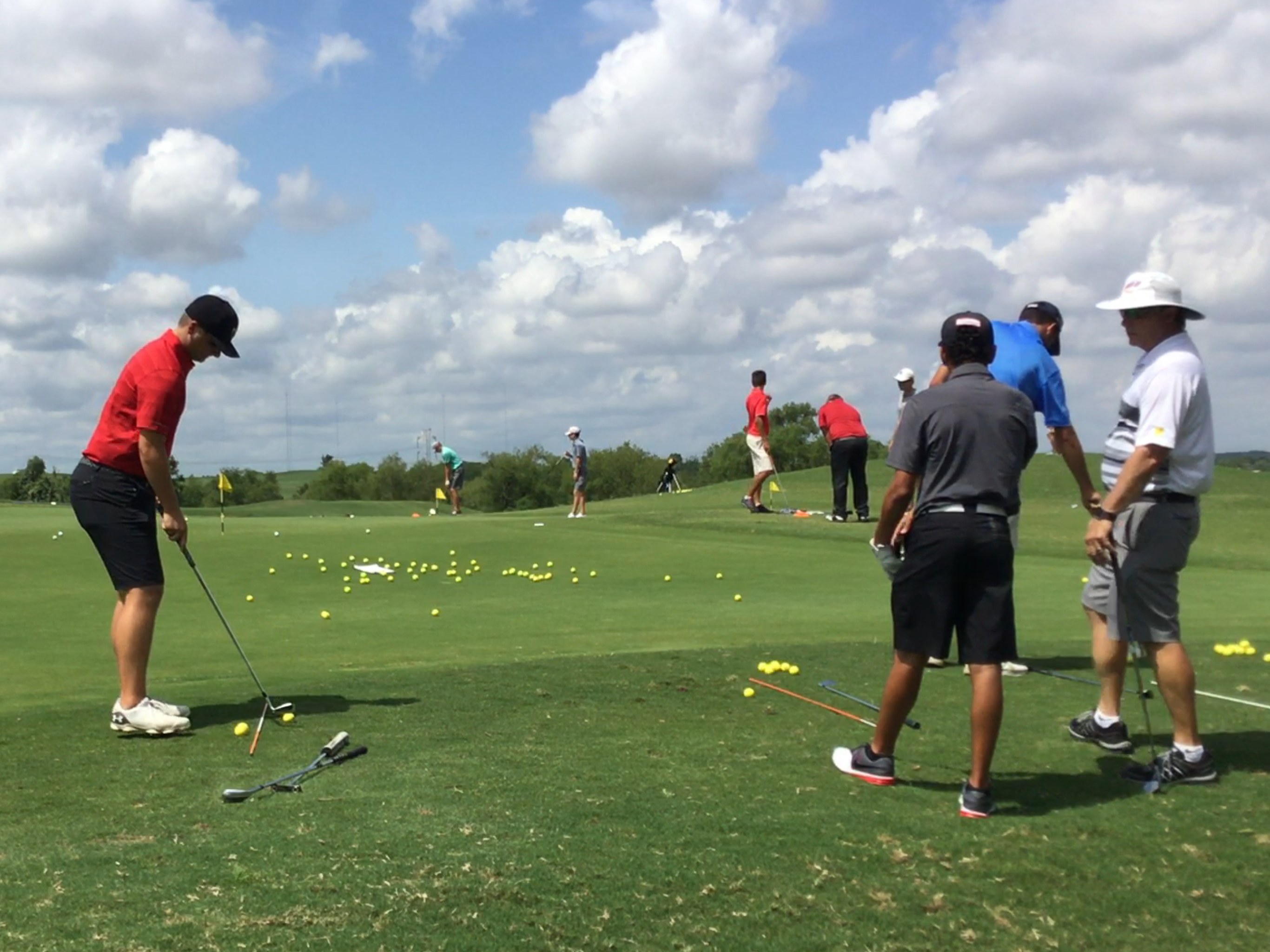 Varsity junior golfers practicing chipping and putting on the course with their coaches